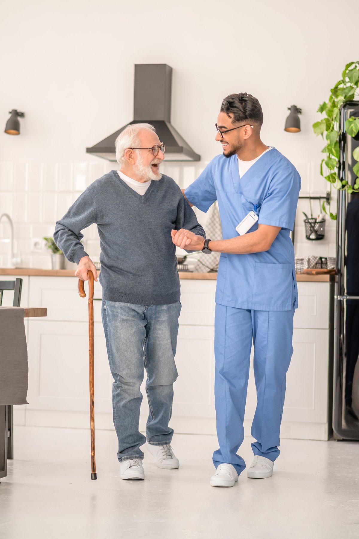 An older man walking with a cane alongside a caregiver who is supporting him