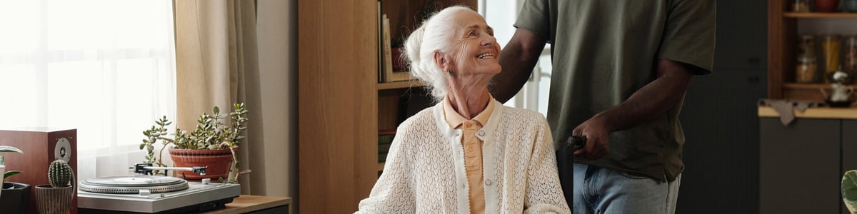 An older woman in a wheelchair smiling as she talks with a younger companion at home
